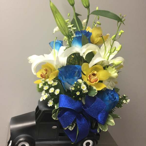 Bouquet of lilies, orchids, and blue roses arranged on a black truck-shaped base