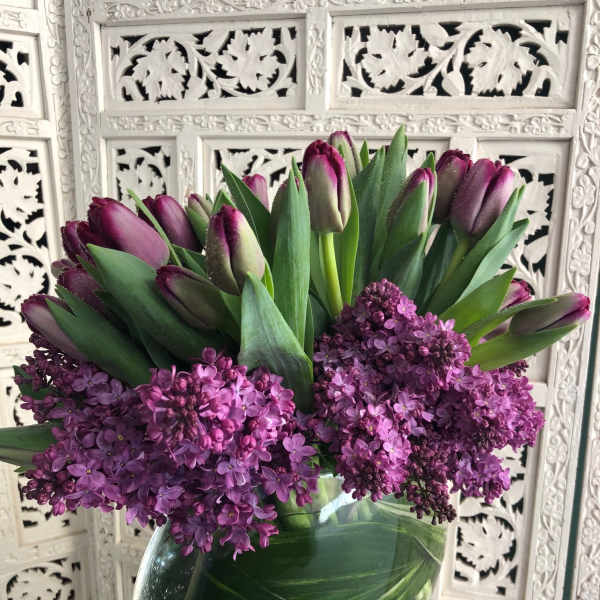 Purple tulips and lilac blooms arranged in a clear glass vase