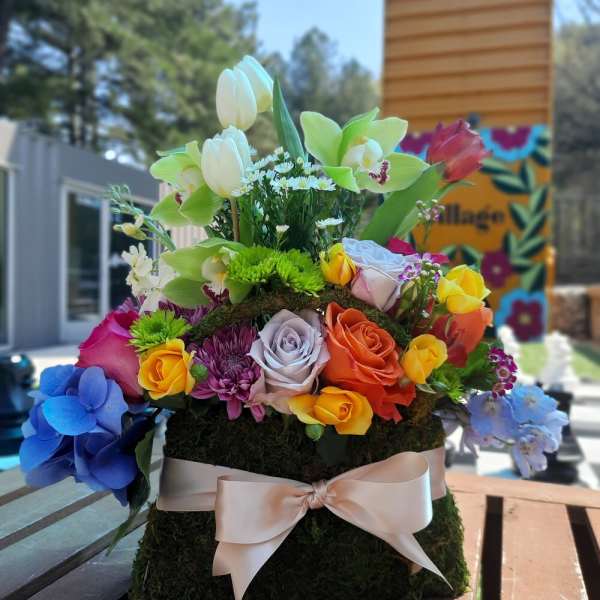Colorful floral arrangement with roses, orchids, tulips, and hydrangeas on a moss base