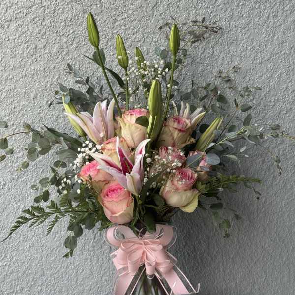 Pink roses and lilies in a glass vase with a pink ribbon