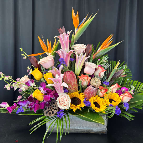Tropical flower arrangement with lilies, roses, orchids, and sunflowers in a wooden box