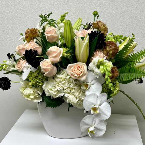 Mixed floral arrangement in a white vase with pale roses and white orchids