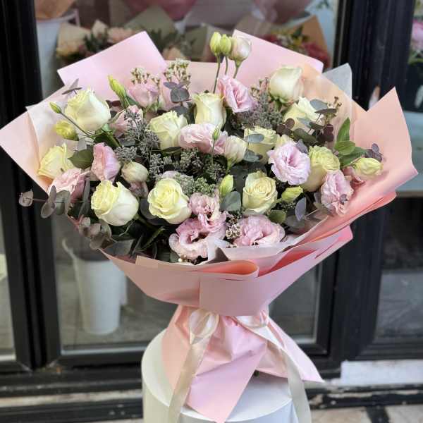 Bouquet of pale pink and cream roses with pink blooms wrapped in pink paper