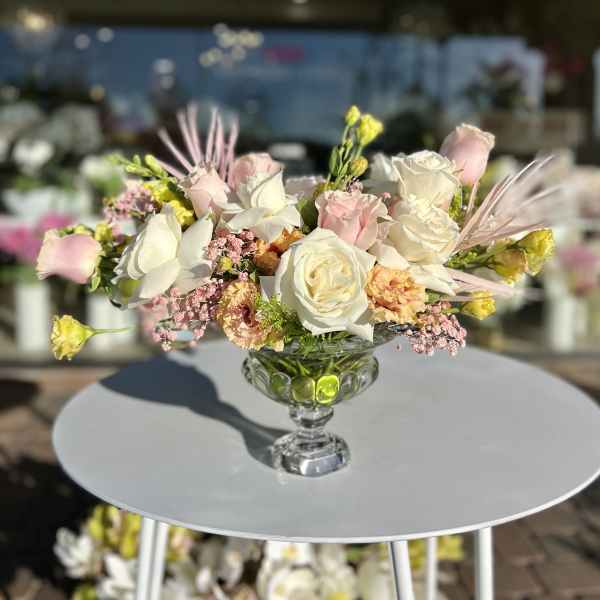Low floral centerpiece with white and blush roses in a glass compote vase