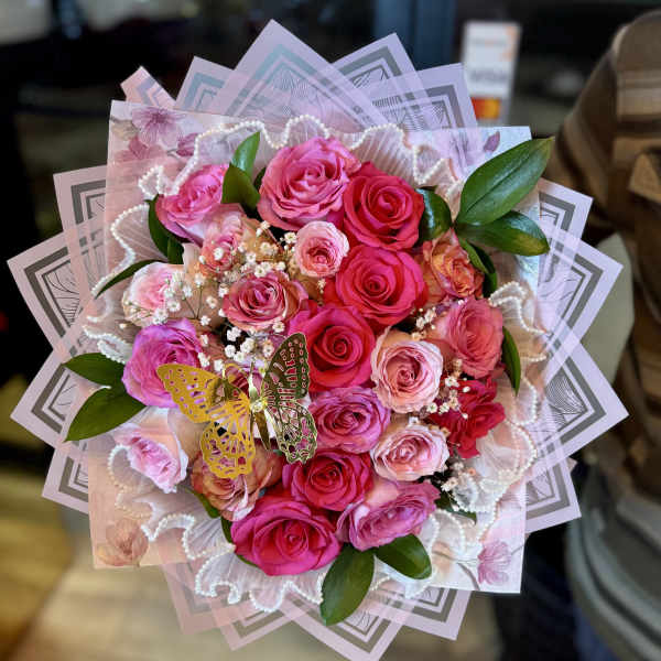 Pink and red rose bouquet with decorative wrapping and a butterfly accent