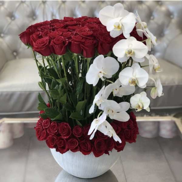 Red roses arranged in a white vase with white orchids