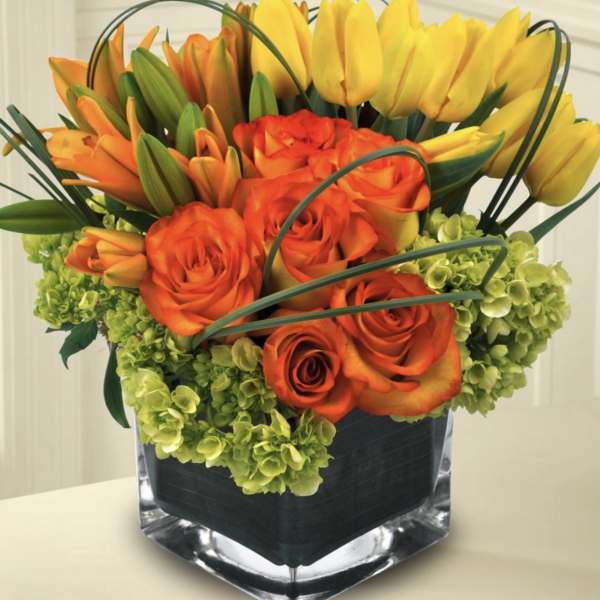 Orange roses and yellow tulips arranged in a square glass vase
