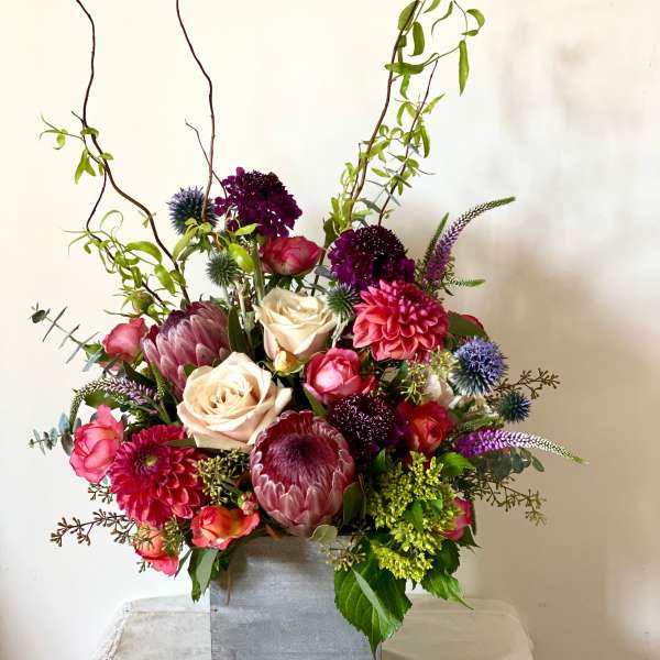 Tall mixed flower arrangement in a square silver vase