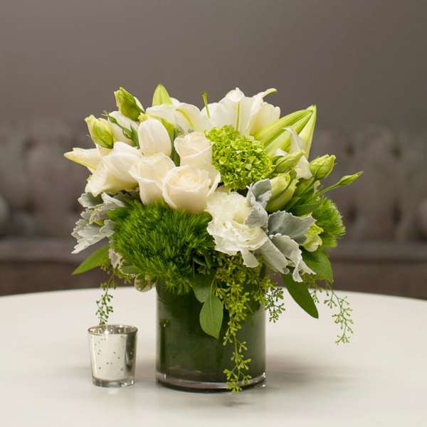 White roses and lilies arranged in a dark glass vase with green accents