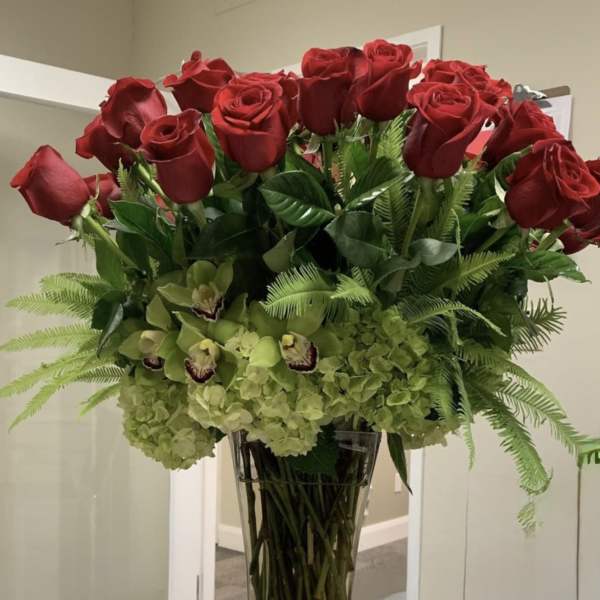 Tall vase arrangement of red roses, green orchids, and hydrangeas