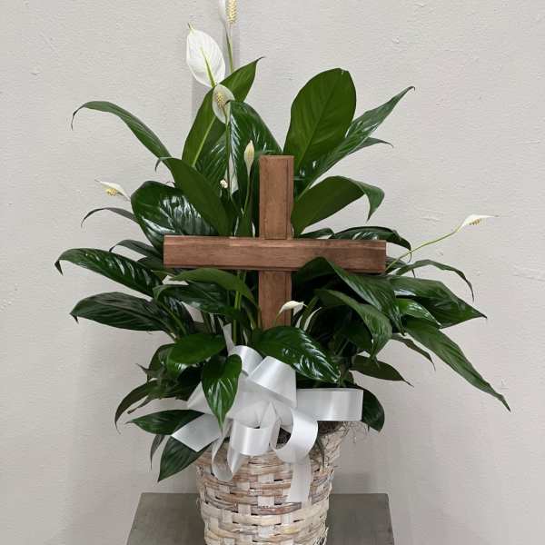 White peace lilies in a wicker basket with a wooden cross and white ribbon