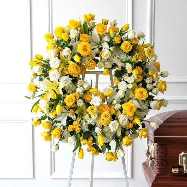 Yellow and white floral wreath on an easel beside a casket