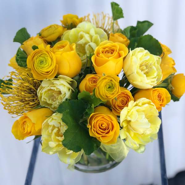 Yellow roses and pale blooms arranged in a clear glass vase