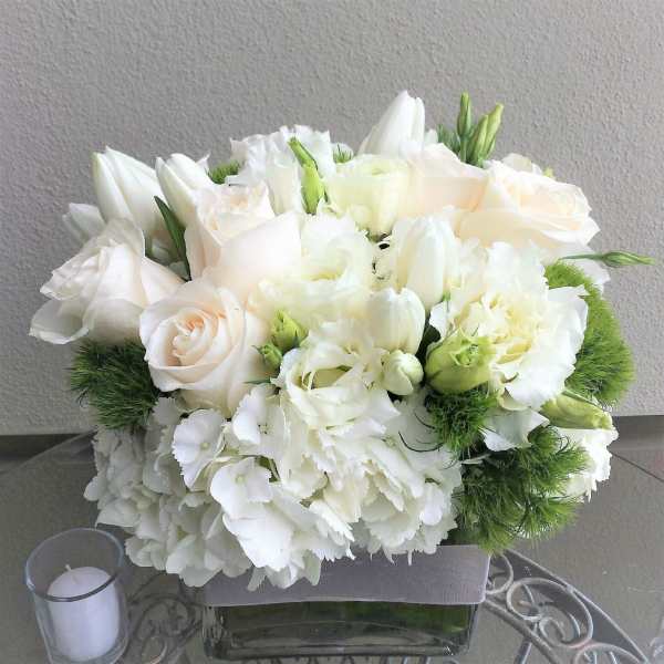 White floral arrangement in a square glass vase with a candle nearby