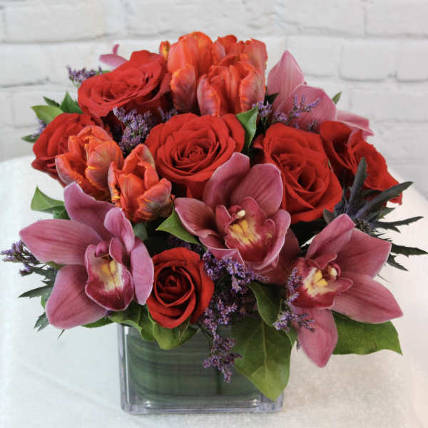 Bouquet of red roses and pink orchids in a square glass vase