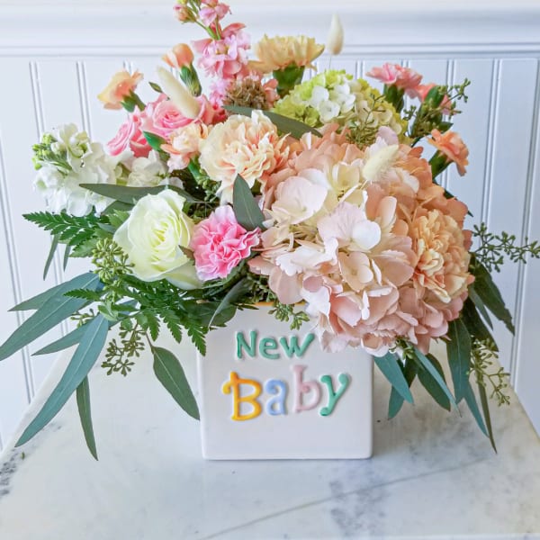 Pastel flower arrangement in a white vase with "New Baby" text