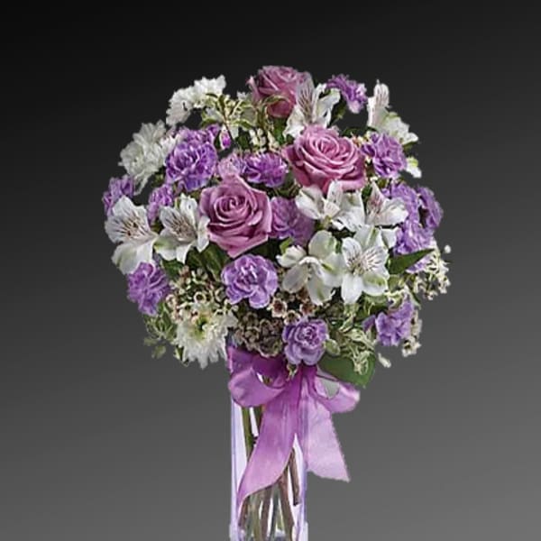 Purple and white bouquet in a clear glass vase with a ribbon
