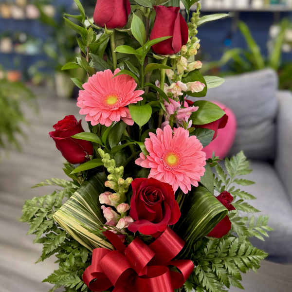 Tall bouquet of red roses and pink gerbera daisies with a red ribbon