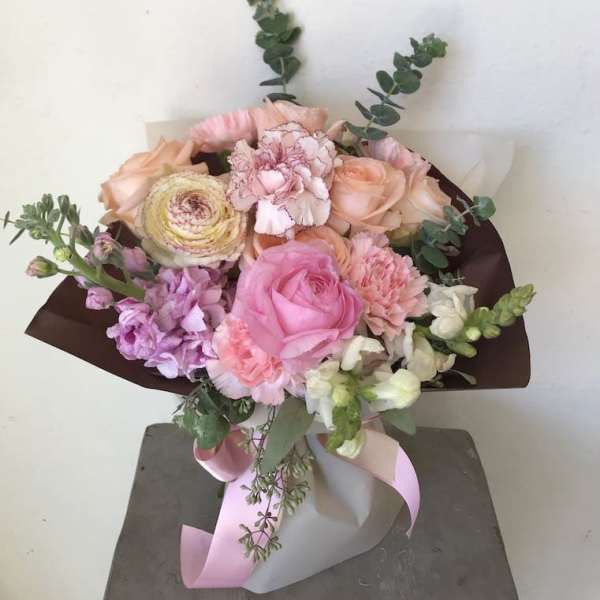 Bouquet of pink, peach, and white flowers wrapped in dark paper with a pink ribbon