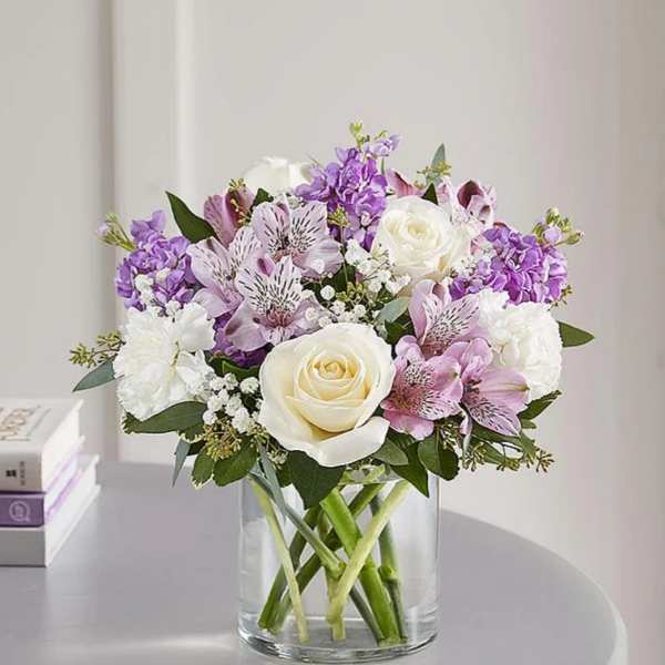 Bouquet of white roses, purple flowers, and pink lilies in a glass vase