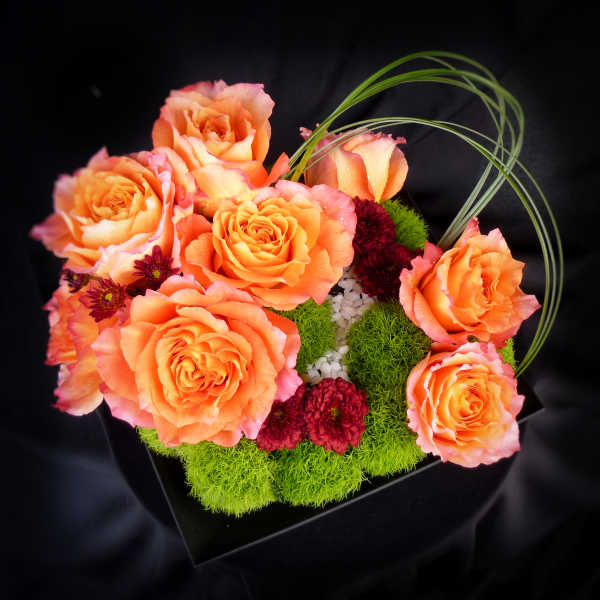 Orange roses arranged in a black square container with green moss and curved grass