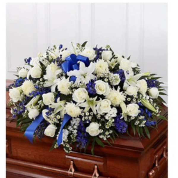 White and blue floral casket spray with ribbon on a wooden casket