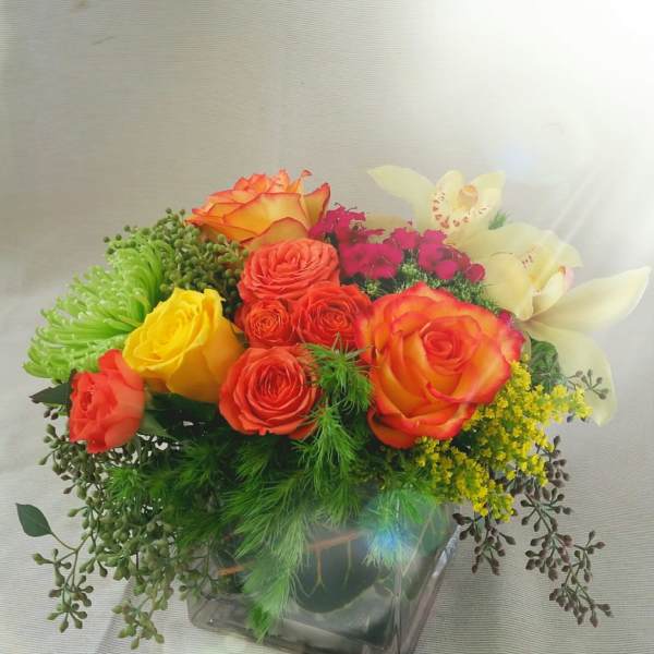 Colorful bouquet of roses and orchids in a square glass vase