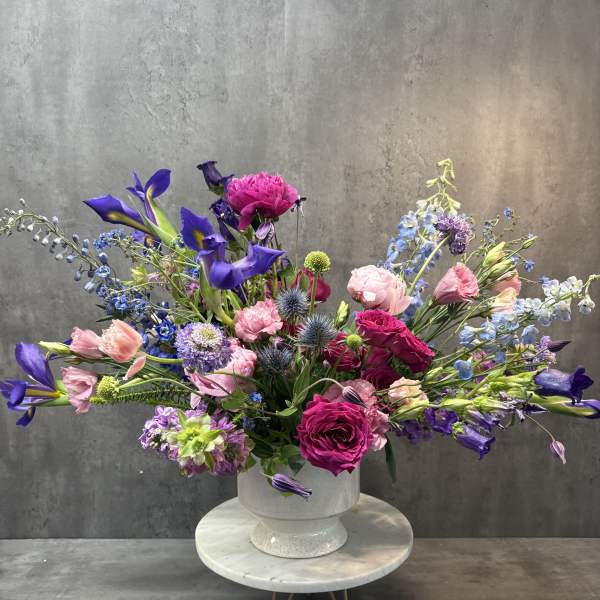 Large mixed bouquet of pink, purple, and blue flowers in a white pedestal vase