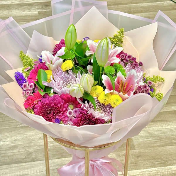Bouquet of pink, white, and yellow flowers wrapped in pale pink paper