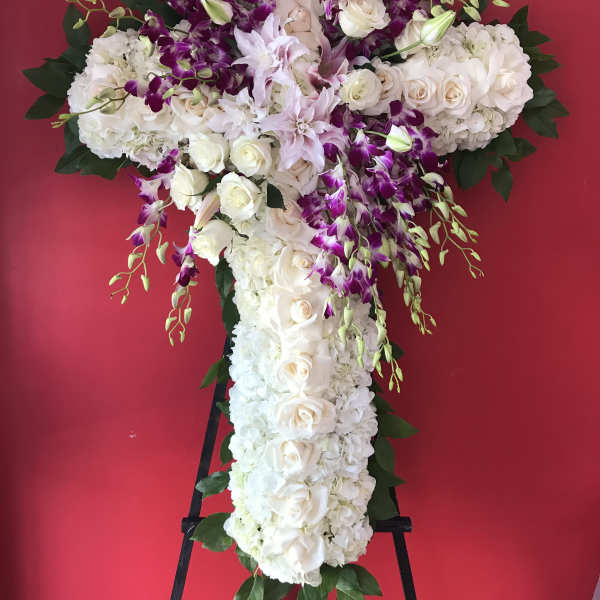 Large white floral cross with purple orchids on a stand