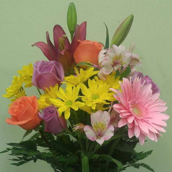 Mixed bouquet of roses, lilies, daisies, and alstroemeria in a glass vase with a pink ribbon