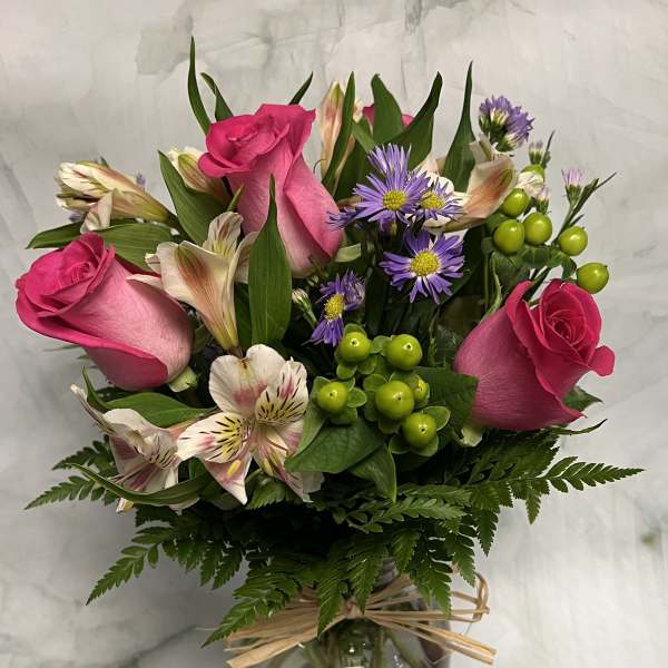Pink roses and purple daisies arranged in a glass vase