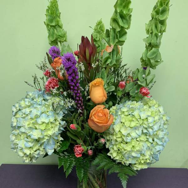 Mixed bouquet in a glass vase with hydrangeas, roses, and tall green spikes