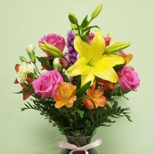 Bouquet of pink roses, yellow lilies, and orange alstroemeria in a glass vase