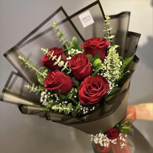 Bouquet of red roses wrapped in dark paper with baby's breath