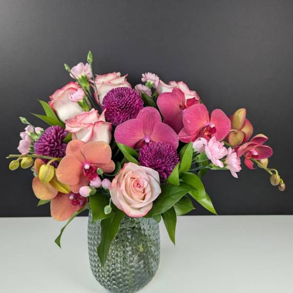 Pink and purple arrangement of roses, orchids, and mums in a textured glass vase
