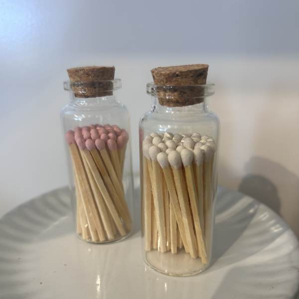 Two glass bottles filled with wooden matches, one with pink tips and one with white tips