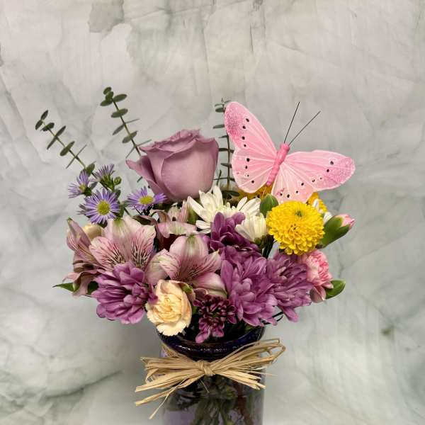 Purple and pink mixed bouquet in a glass vase with a pink butterfly pick