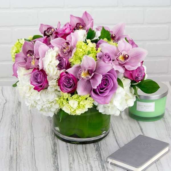 Pink orchids and roses arranged in a green glass vase with white blooms