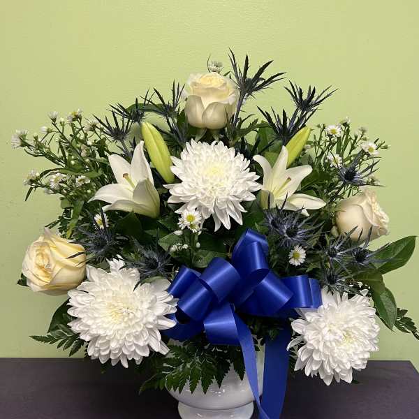 White roses and lilies arranged with chrysanthemums in a white vase with a blue ribbon
