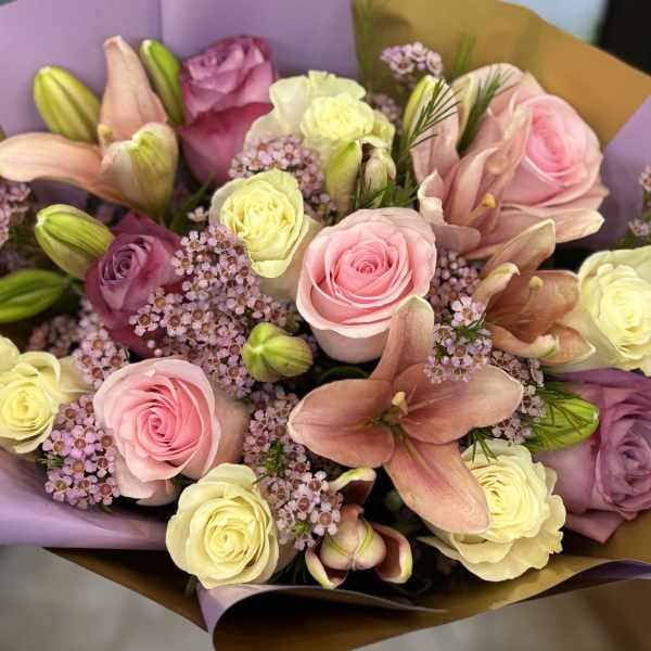Bouquet of pink and cream roses with lilies wrapped in purple and gold paper