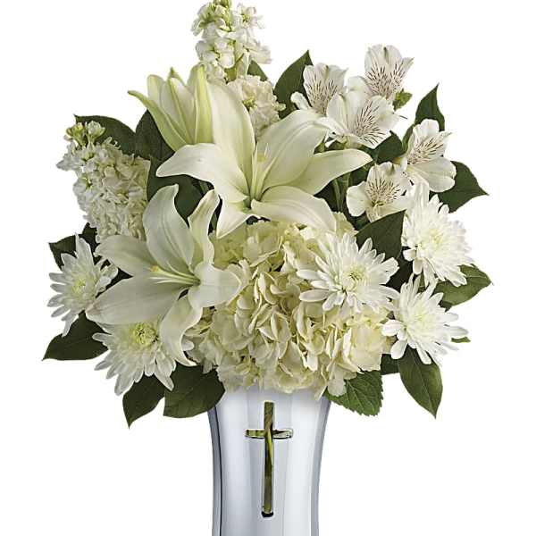 White lilies and daisies arranged in a silver vase with a cross cutout