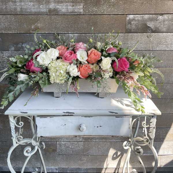 Long floral arrangement of pink, coral, and white roses in a white container