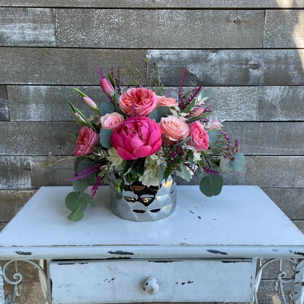 Pink floral arrangement in a silver vase on a white table