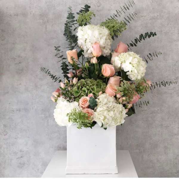 White hydrangeas and peach roses in a white box with eucalyptus