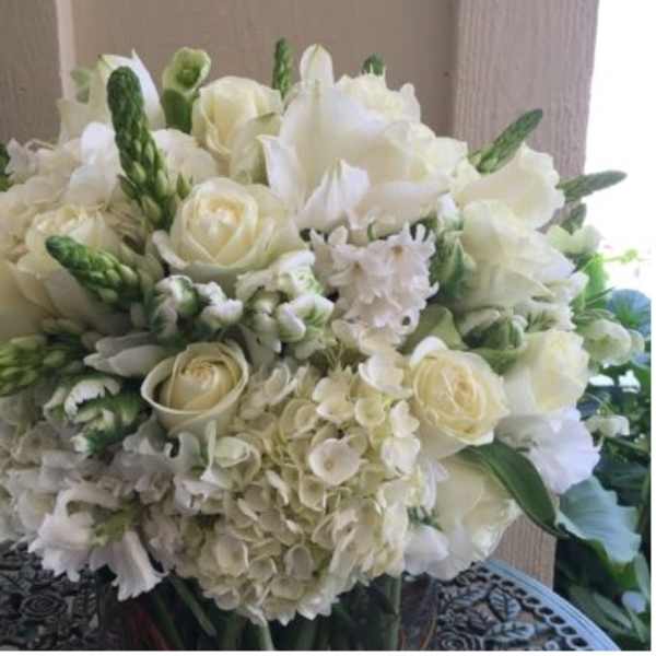 Round arrangement of white roses and hydrangeas with green buds in a clear glass vase