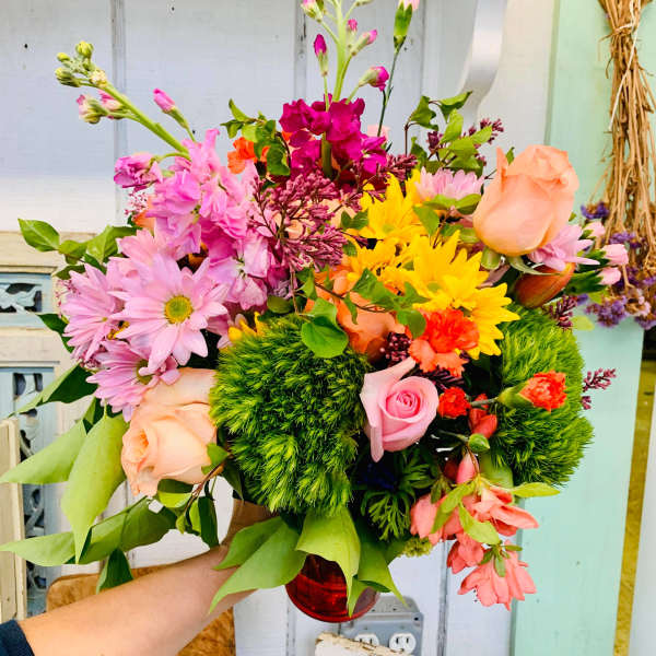Mixed bouquet of pink, peach, and yellow flowers in a red vase