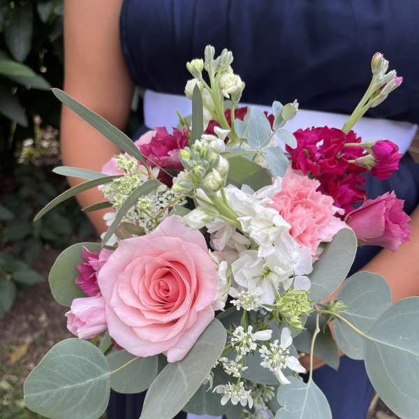 Hand-tied bouquet of pink roses, carnations, and white blooms with eucalyptus, held against a navy dress.