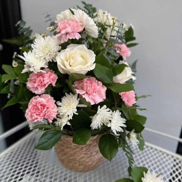 Pink carnations and white daisies arranged in a woven basket