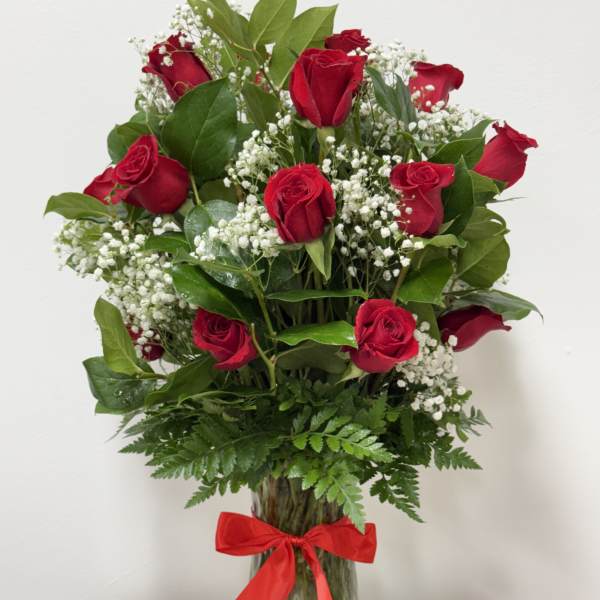 Red roses arranged in a clear glass vase with baby's breath and a red ribbon